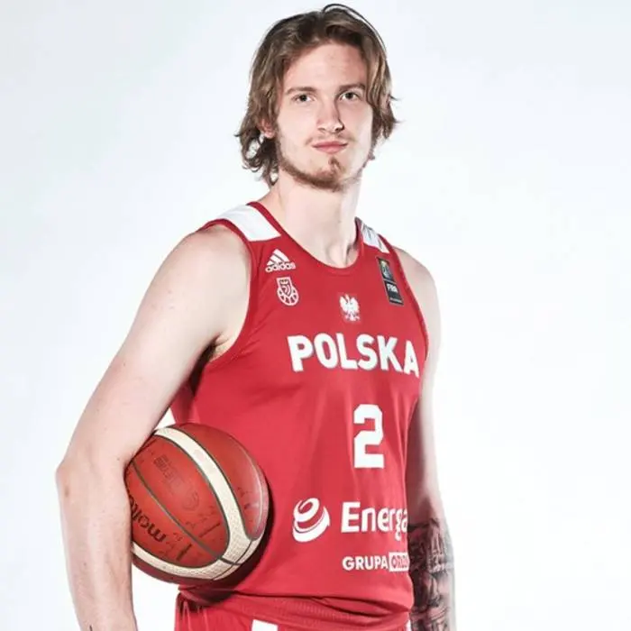 Aleksander Balcerowski in a red Poland national basketball team jersey holding a basketball