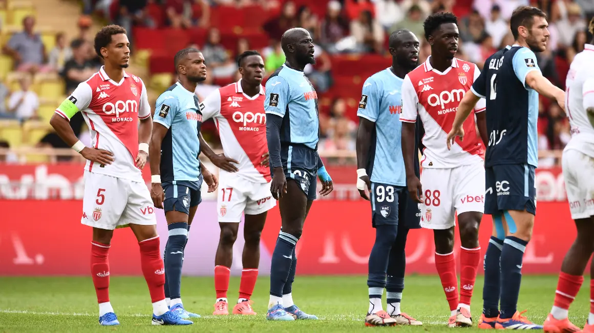 AS Monaco football players in red and white and light blue kits standing on the pitch during a match