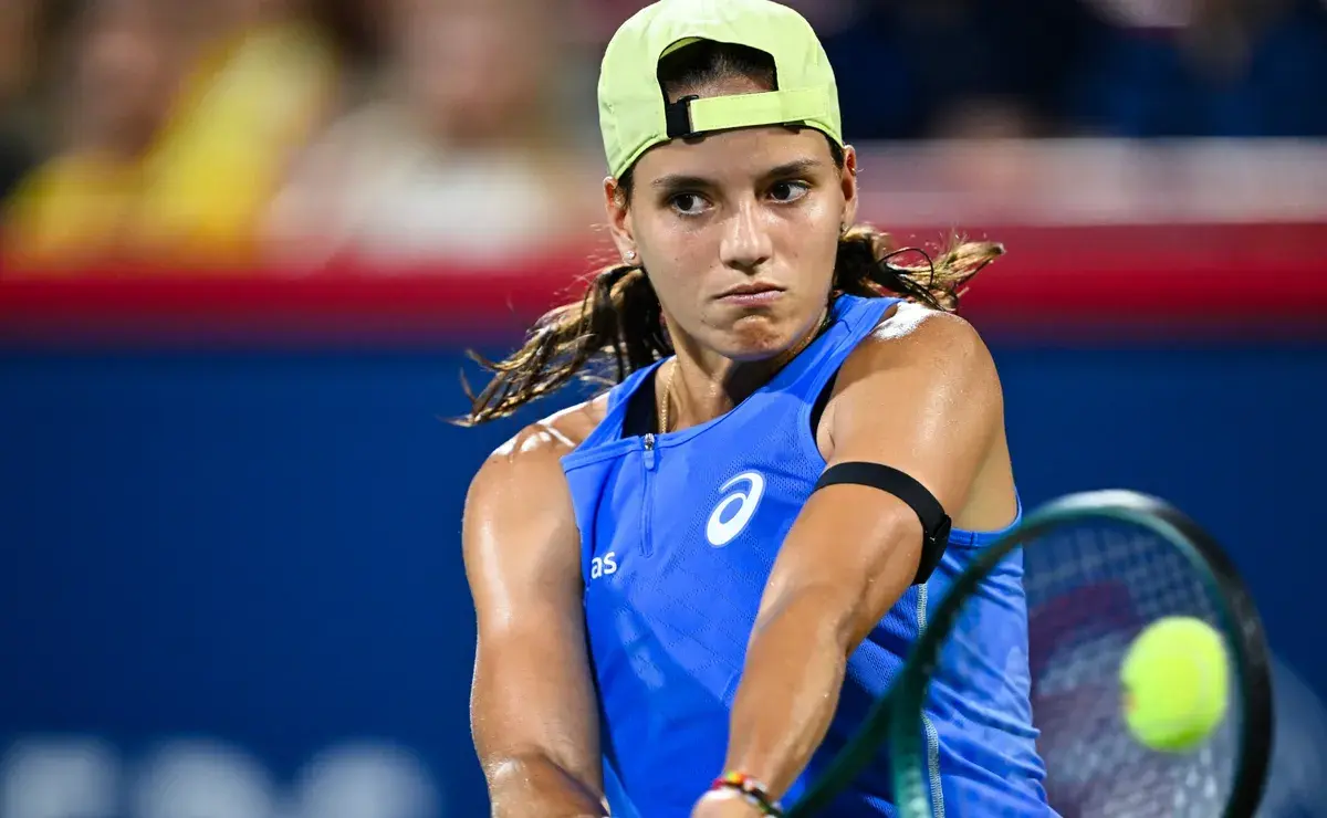 Tennis player Emiliana Arango in a blue outfit and lime green cap hitting a forehand shot.