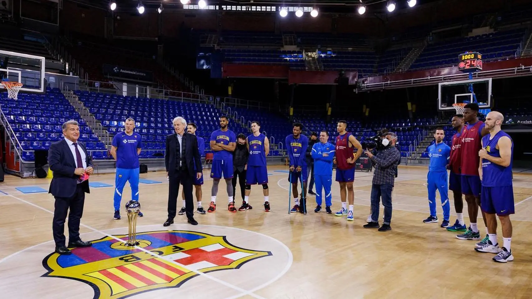 FC Barcelona basketball players and staff standing on the court at Palau Blaugrana with a trophy