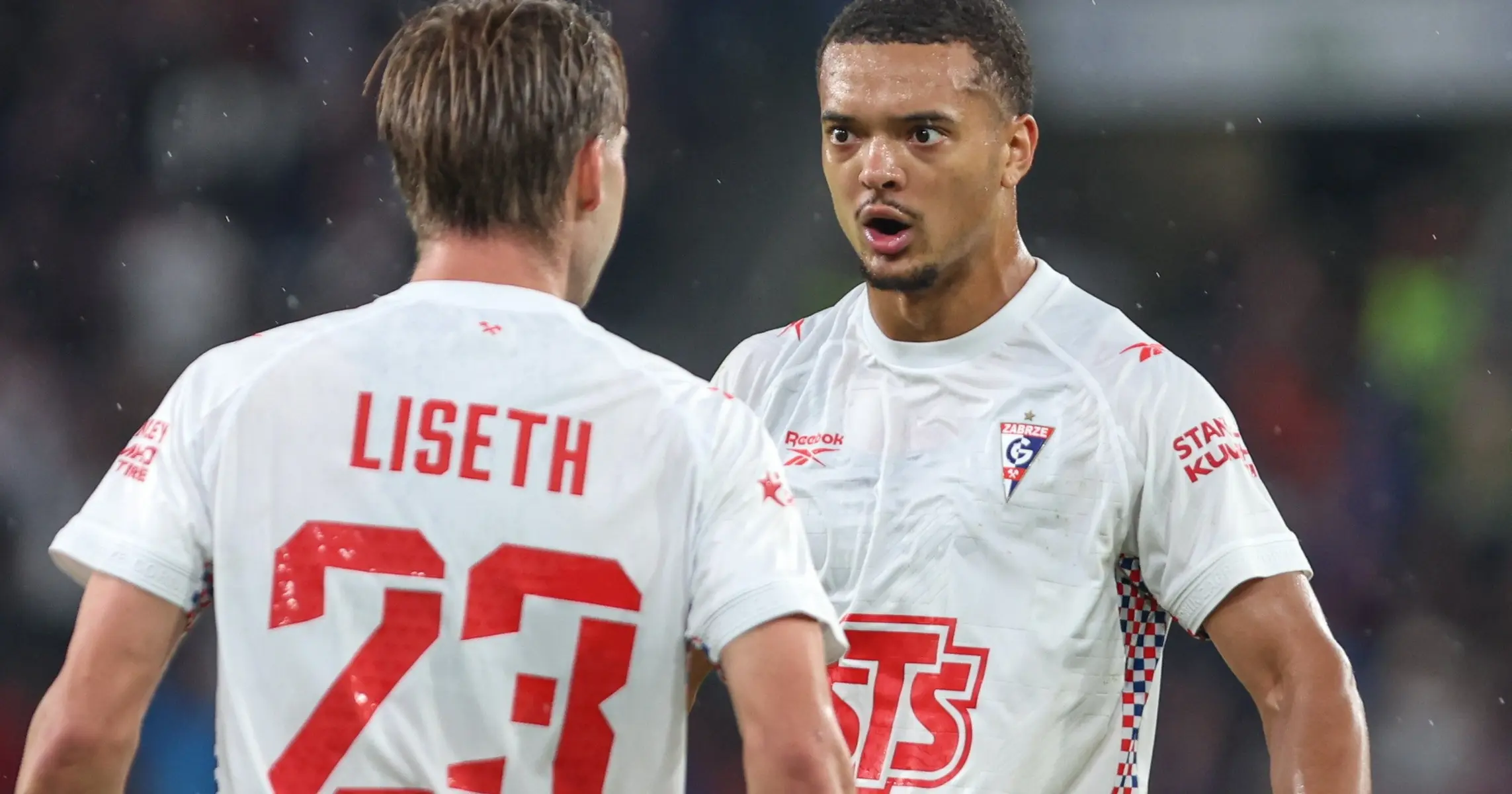 Two Górnik Zabrze football players in white jerseys talking during a match