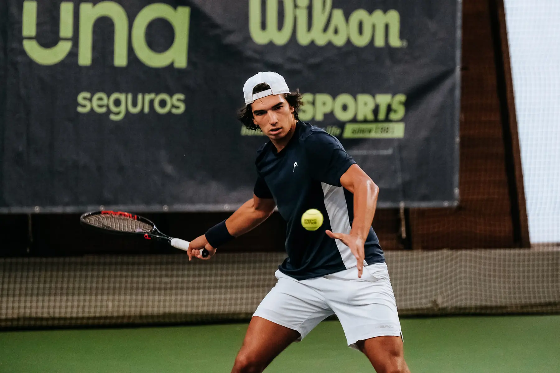 Tennis player Henrique Rocha hitting a forehand shot on a green hard court