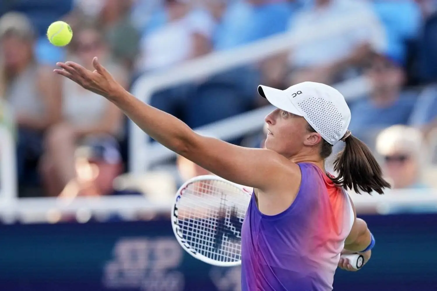 Iga Świątek tossing a tennis ball into the air to serve during a match.