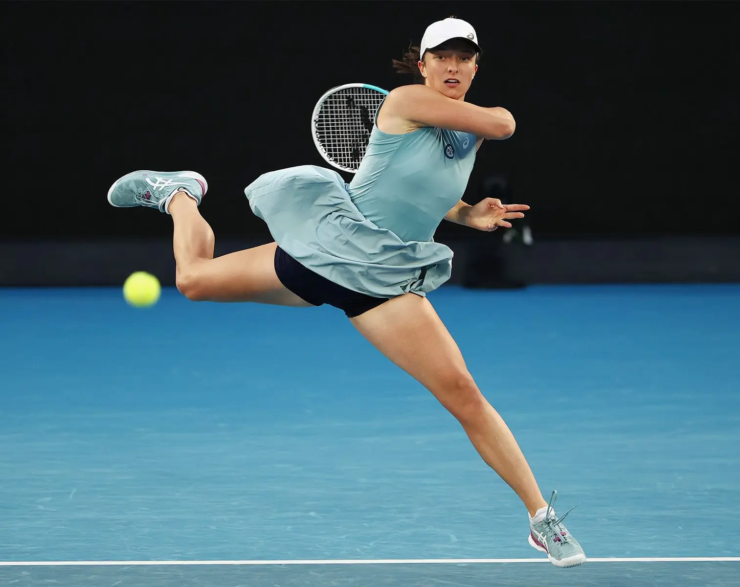 Iga Świątek hitting a tennis ball during a match on a blue hard court