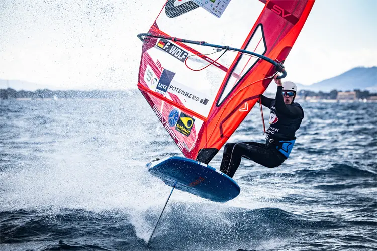 Windsurfer F. Wolf on an iQFOiL board lifting out of the water during a race