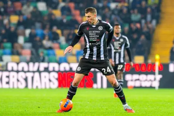 Jakub Piotrowski in a black and white striped Udinese Calcio kit controlling a soccer ball during a match