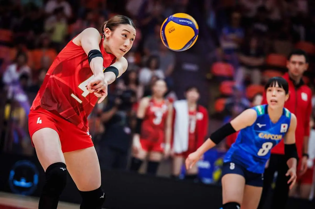 A Japanese female volleyball player in a red uniform bumping a volleyball during a match.