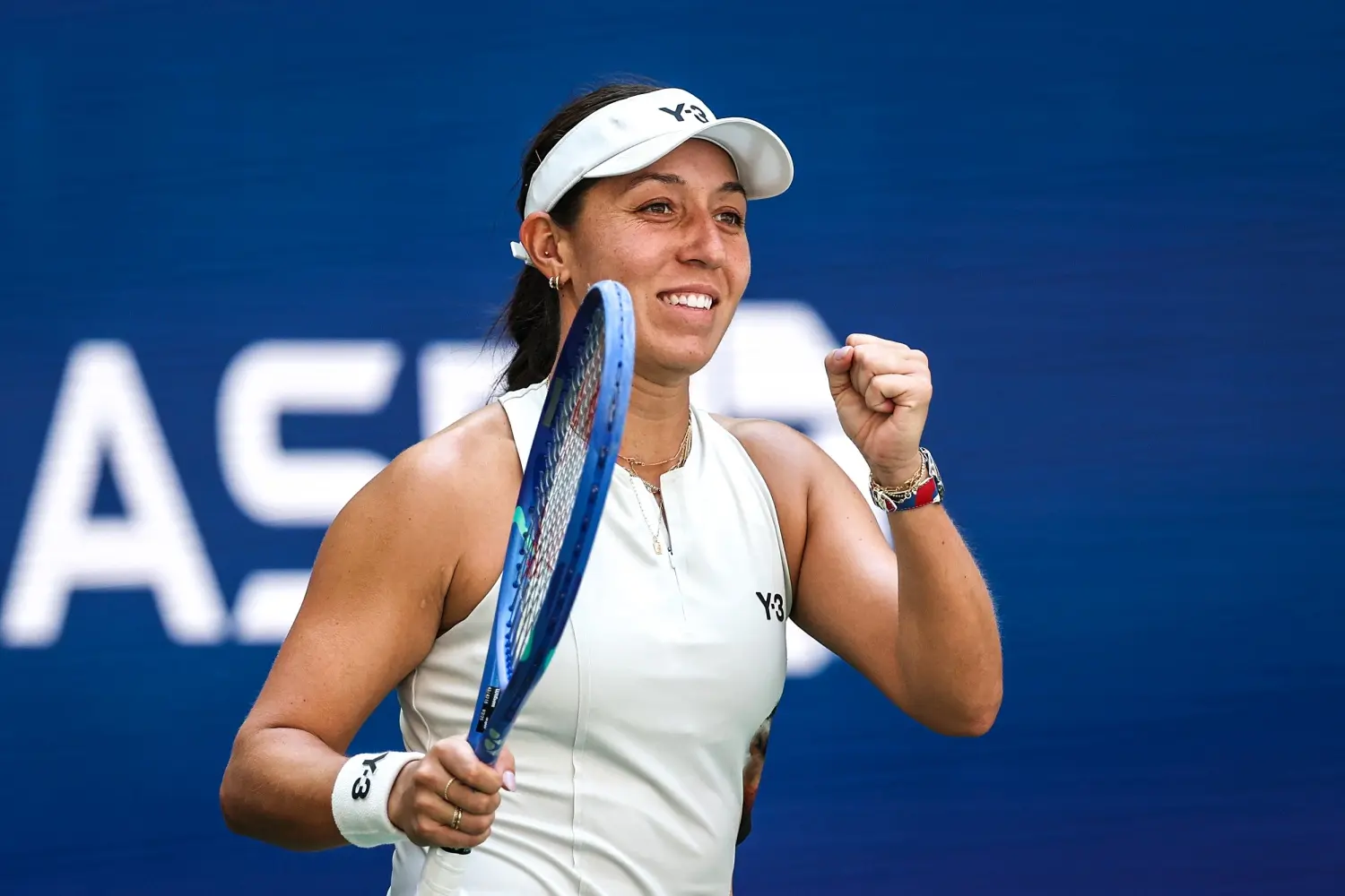 Jessica Pegula in white tennis attire holding a racket and pumping her fist on a tennis court.