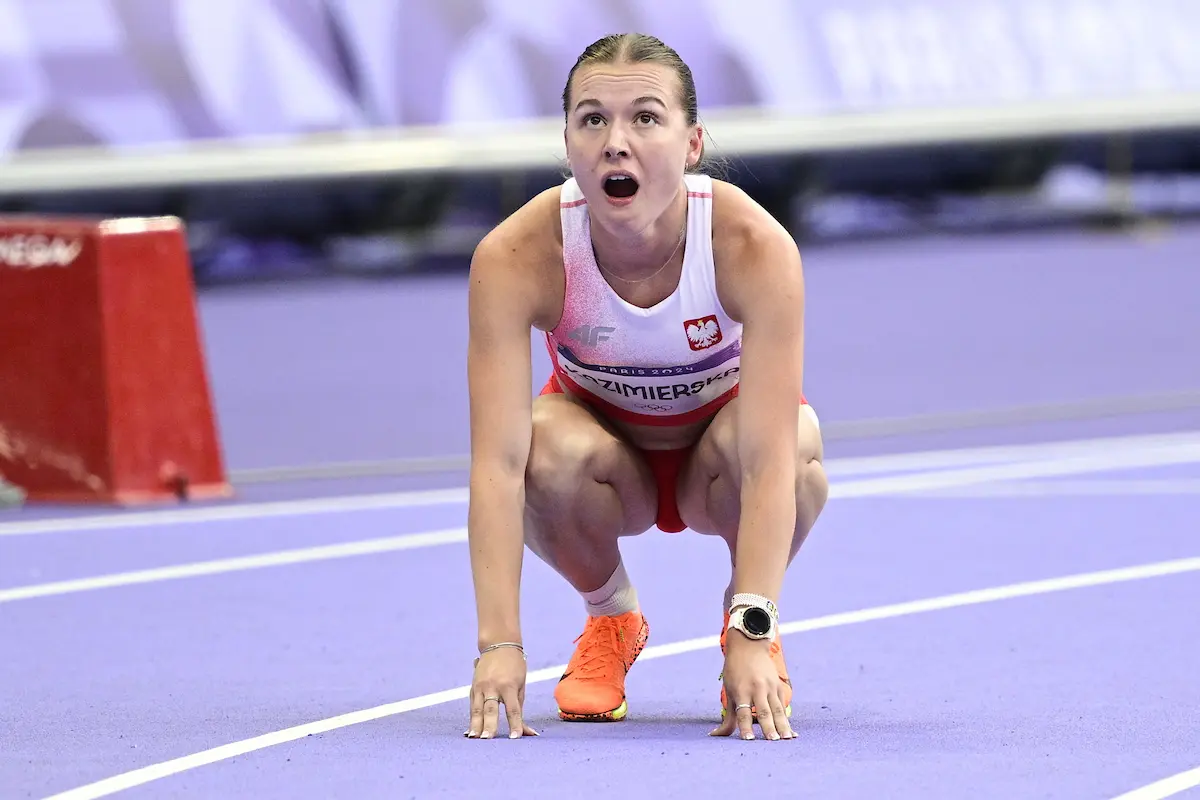 Klaudia Kazimierska in a white and red Polish athletics kit at the starting blocks on a purple track