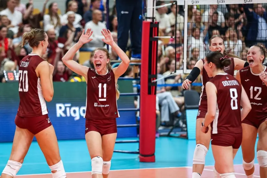 Latvia women's national volleyball team players in maroon uniforms celebrating on the court