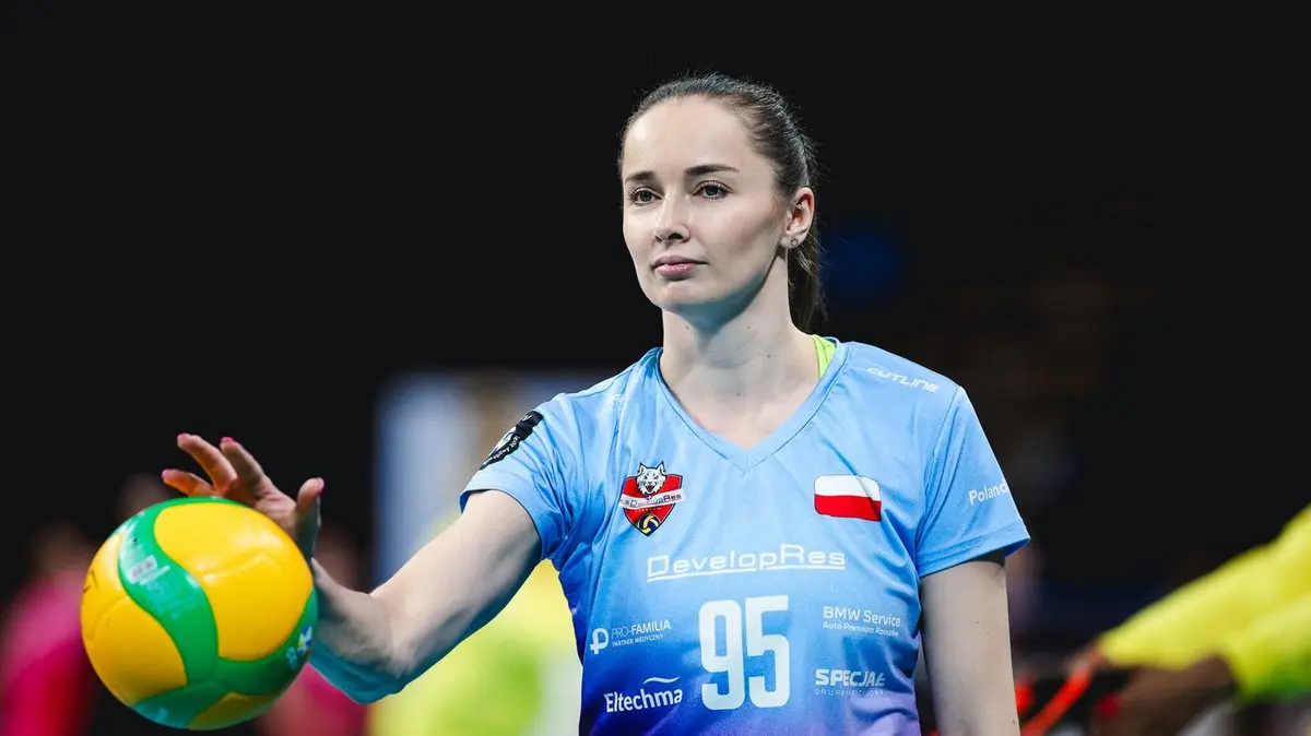 Magdalena Jurczyk in a light blue DevelopRes Rzeszów volleyball jersey holding a yellow and green ball