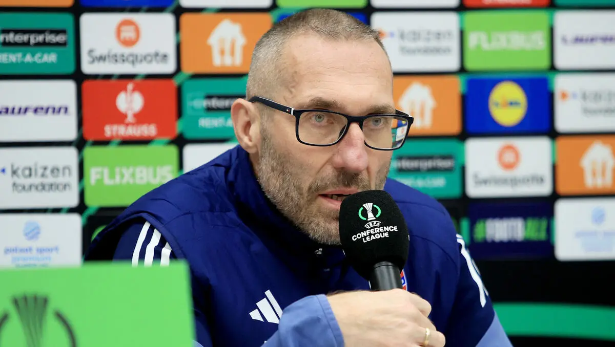 Marek Papszun wearing glasses and a navy blue jacket speaking into a Conference League microphone