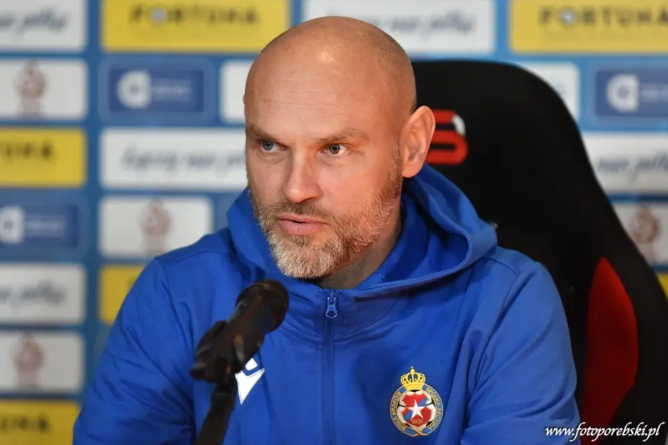 Portrait of Mariusz Jop wearing a blue athletic jacket with a club crest at a press conference