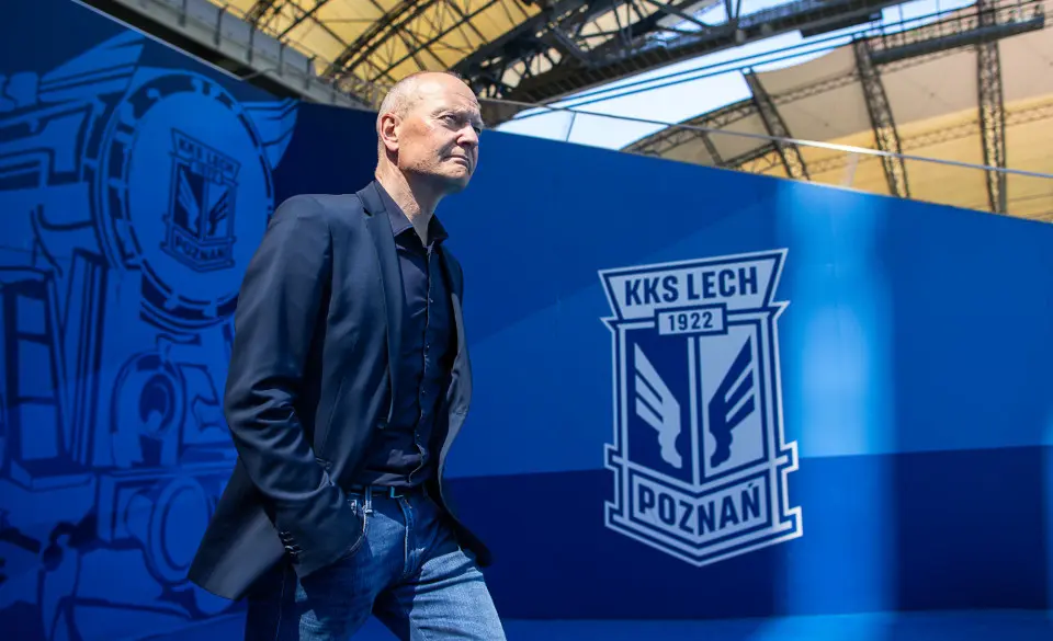 Niels Frederiksen in a navy blazer and jeans standing in front of a blue KKS Lech Poznań wall