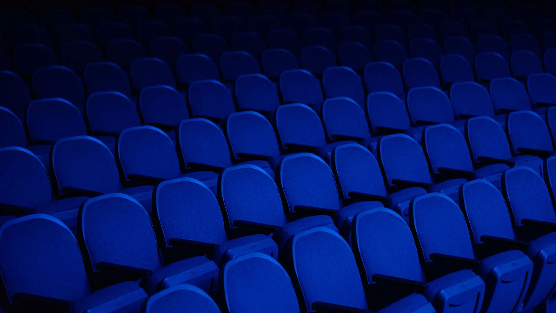 Rows of empty blue plastic stadium seats in a dimly lit arena