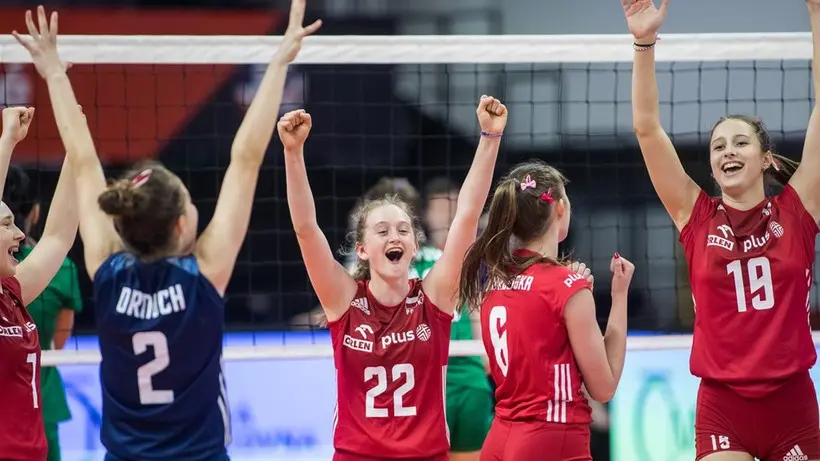 Polish women's U17 volleyball players in red uniforms celebrating a point on the court.