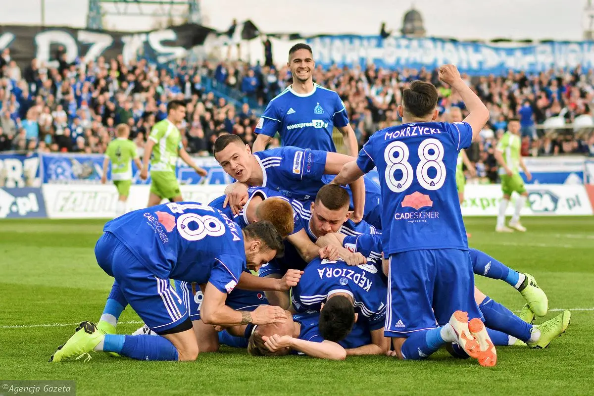 Ruch Chorzów football players in blue jerseys celebrating a goal in a pile on the grass