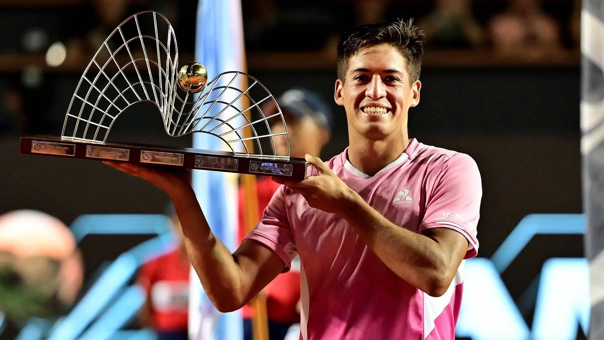 Sebastian Baez smiling and holding a silver trophy after a tennis match