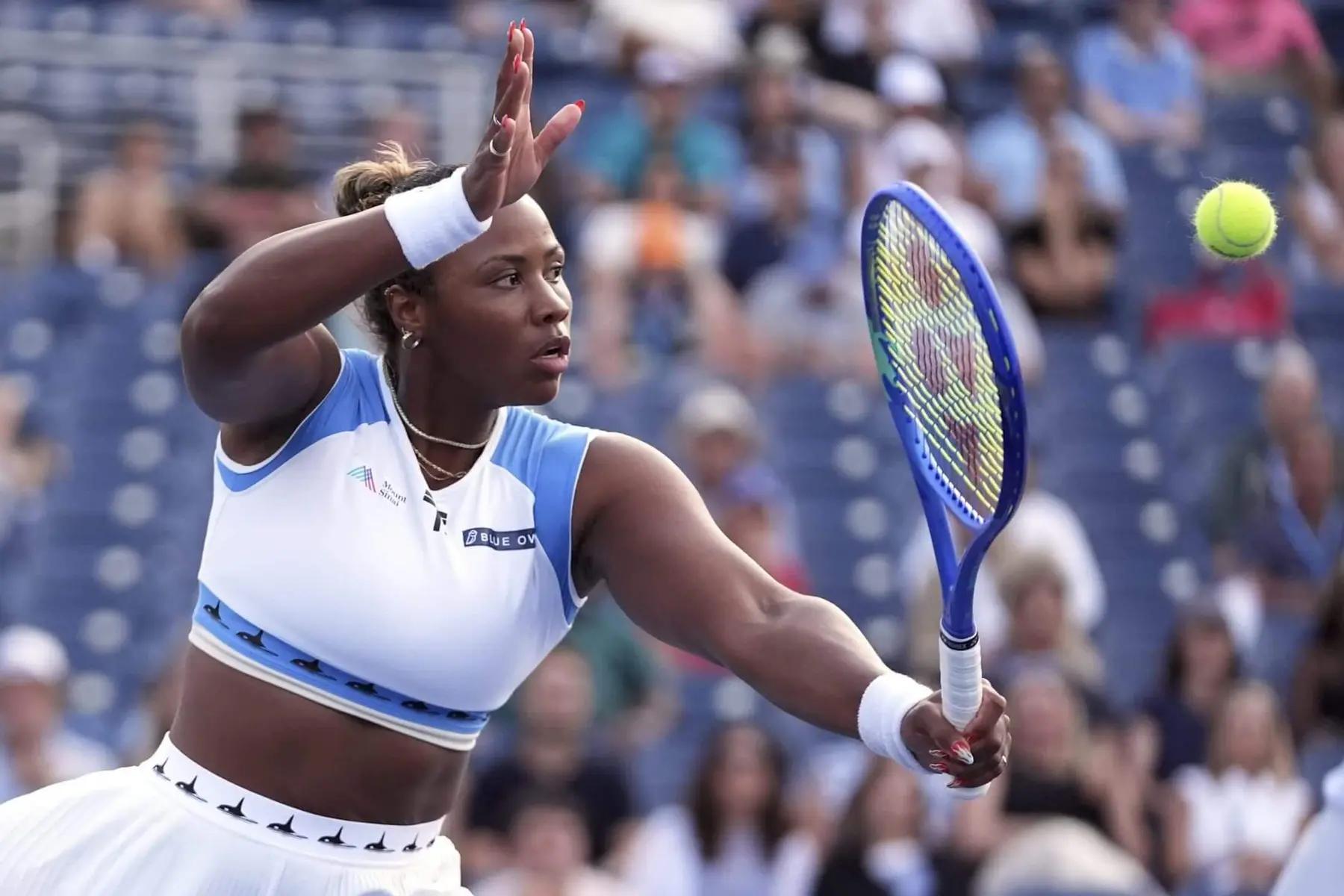 Tennis player Taylor Townsend hitting a forehand shot with a blue racket during a match.