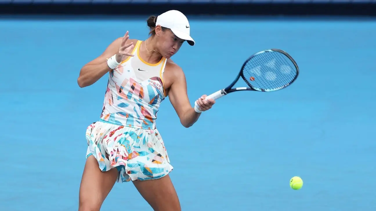 Tennis player Xiyu Wang in a colorful outfit and white cap hitting a tennis ball on a blue court