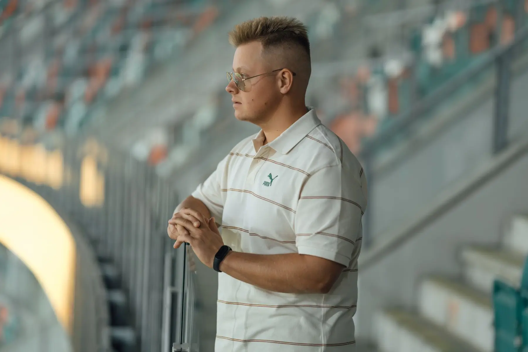 Adrian Siemieniec wearing sunglasses and a white polo shirt standing in a stadium.
