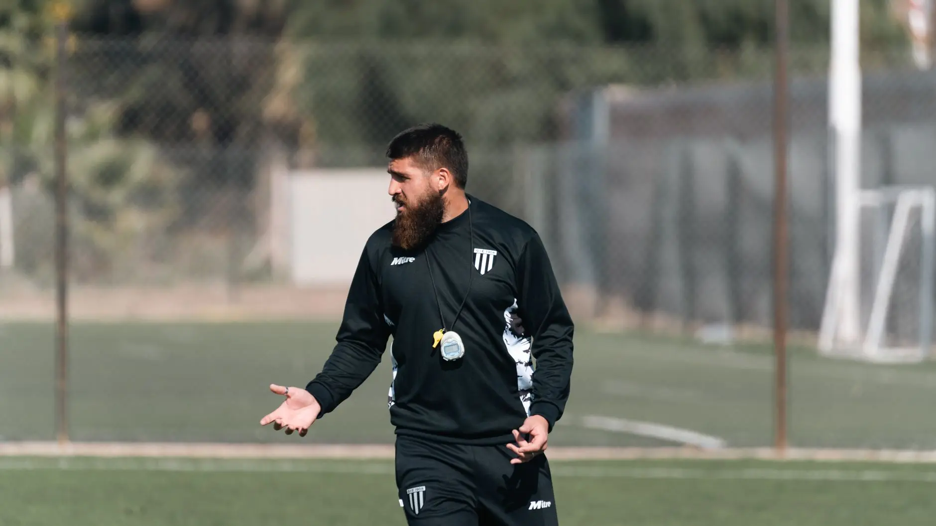 Aleksandar Vukovic in black coaching gear and a whistle on a soccer field.