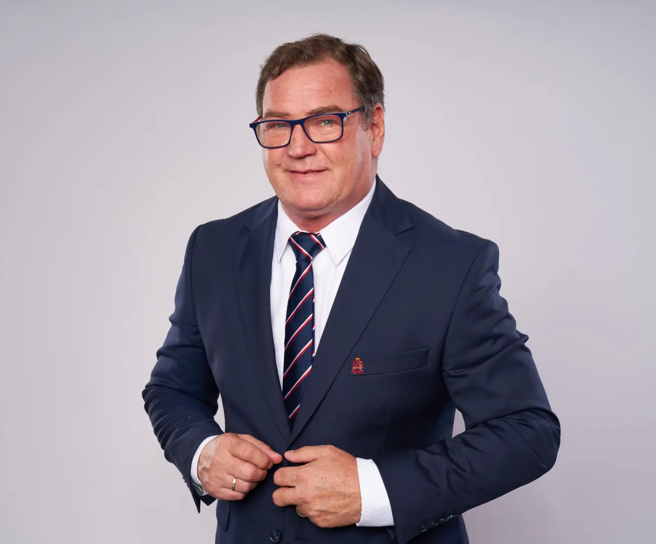 Portret Jana Urbana w ciemnoniebieskim garniturze i okularach.