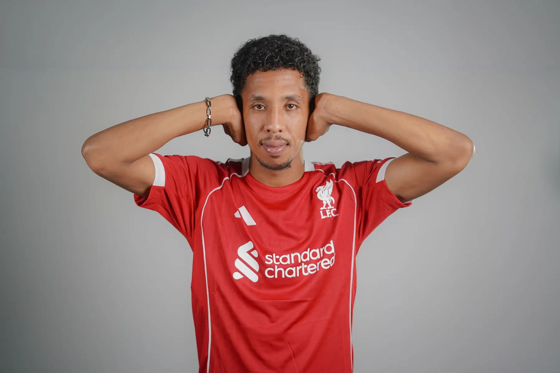 A man wearing a red Liverpool FC jersey with Standard Chartered sponsorship covering his ears
