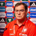 Jan Urban w czerwonej koszulce reprezentacji Polski na tle ścianki sponsorskiej podczas konferencji prasowej