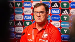 Jan Urban w czerwonej koszulce reprezentacji Polski na tle ścianki sponsorskiej podczas konferencji prasowej