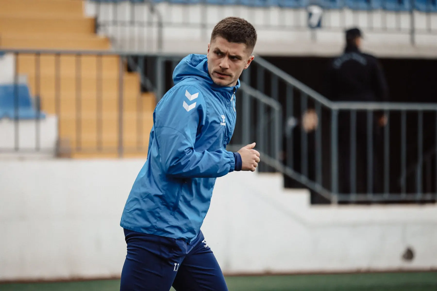 Szymon Marciniak wearing a blue athletic jacket on a football pitch