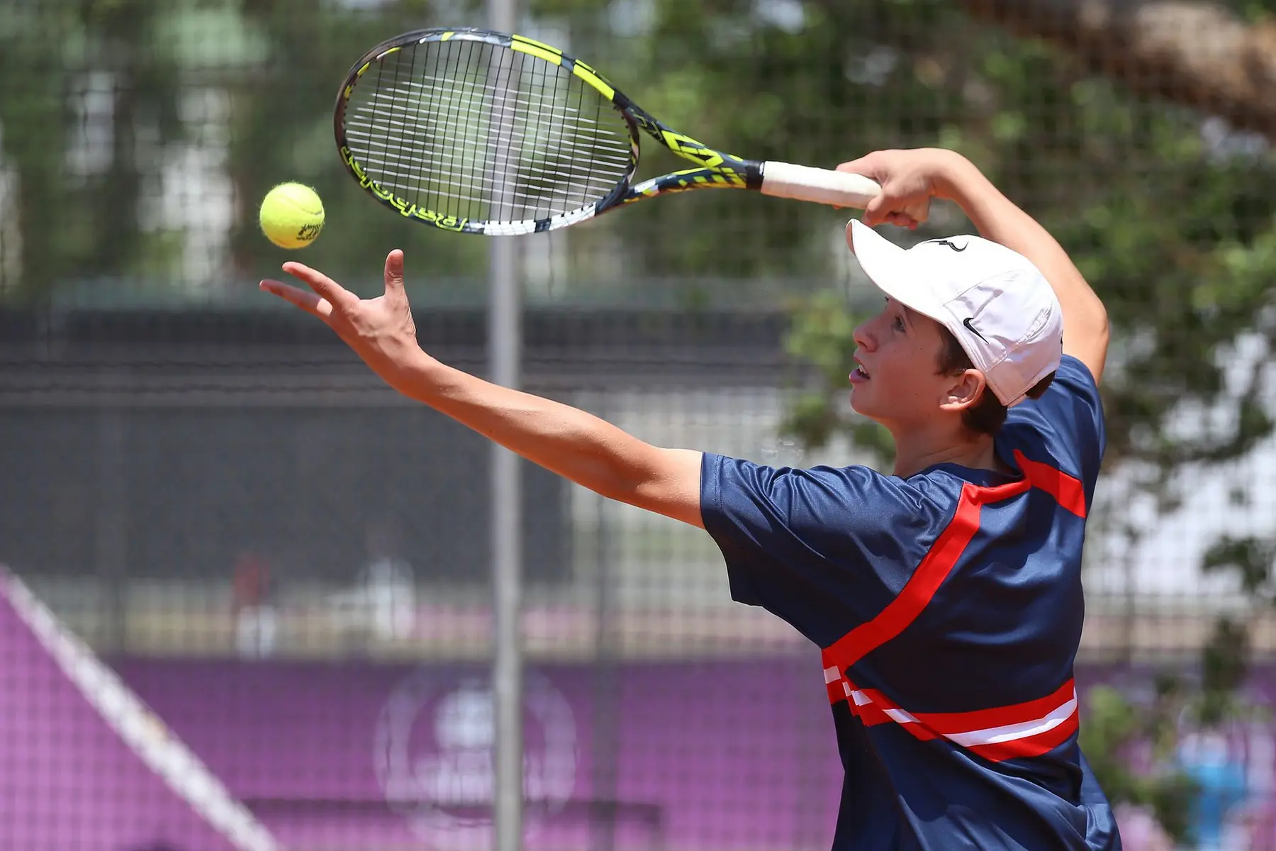 Tennis player Valentin Vacherot tossing a ball into the air to serve on a clay court